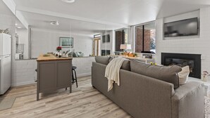 A modern kitchen with white brick walls, a wooden island, and a grey sofa. - Great Location for Year-Round Recreation & Luxury Community Amenities + Pet-Friendly! (Park City)
