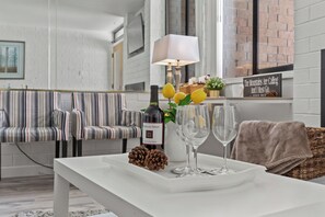 Un salon moderne avec des canapés à rayures, une table basse blanche sur laquelle se trouvent une bouteille, des verres et une pomme de pin.