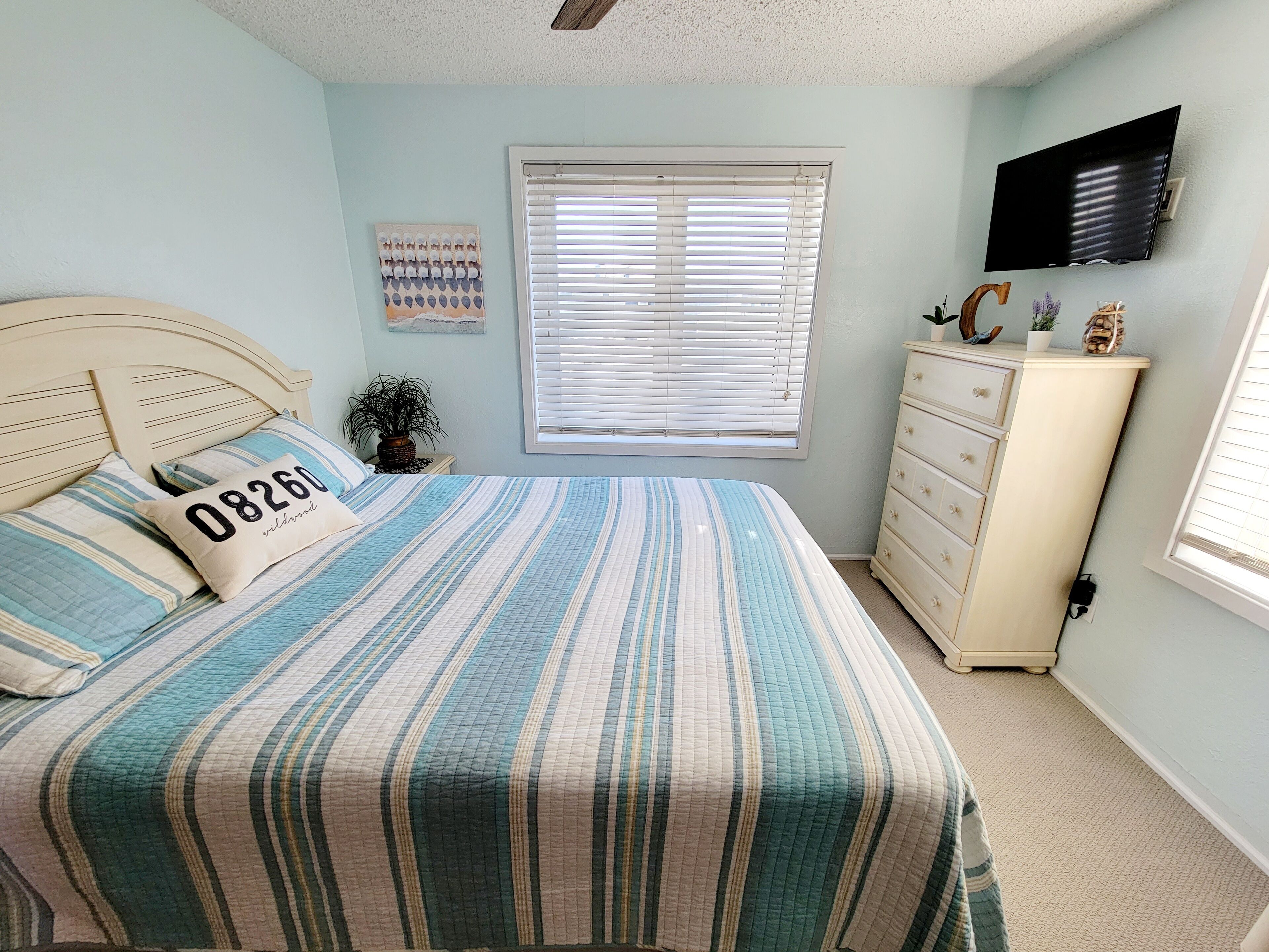 A bedroom with a bed, a dresser, a television, and a window with blinds.