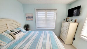 Un dormitorio con cama, cómoda, televisor y ventana con persianas.