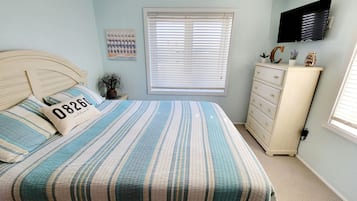 A bedroom with a bed, a dresser, a television, and a window with blinds.