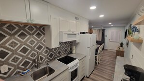 Una cocina compacta con armarios blancos, microondas, estufa y refrigerador.