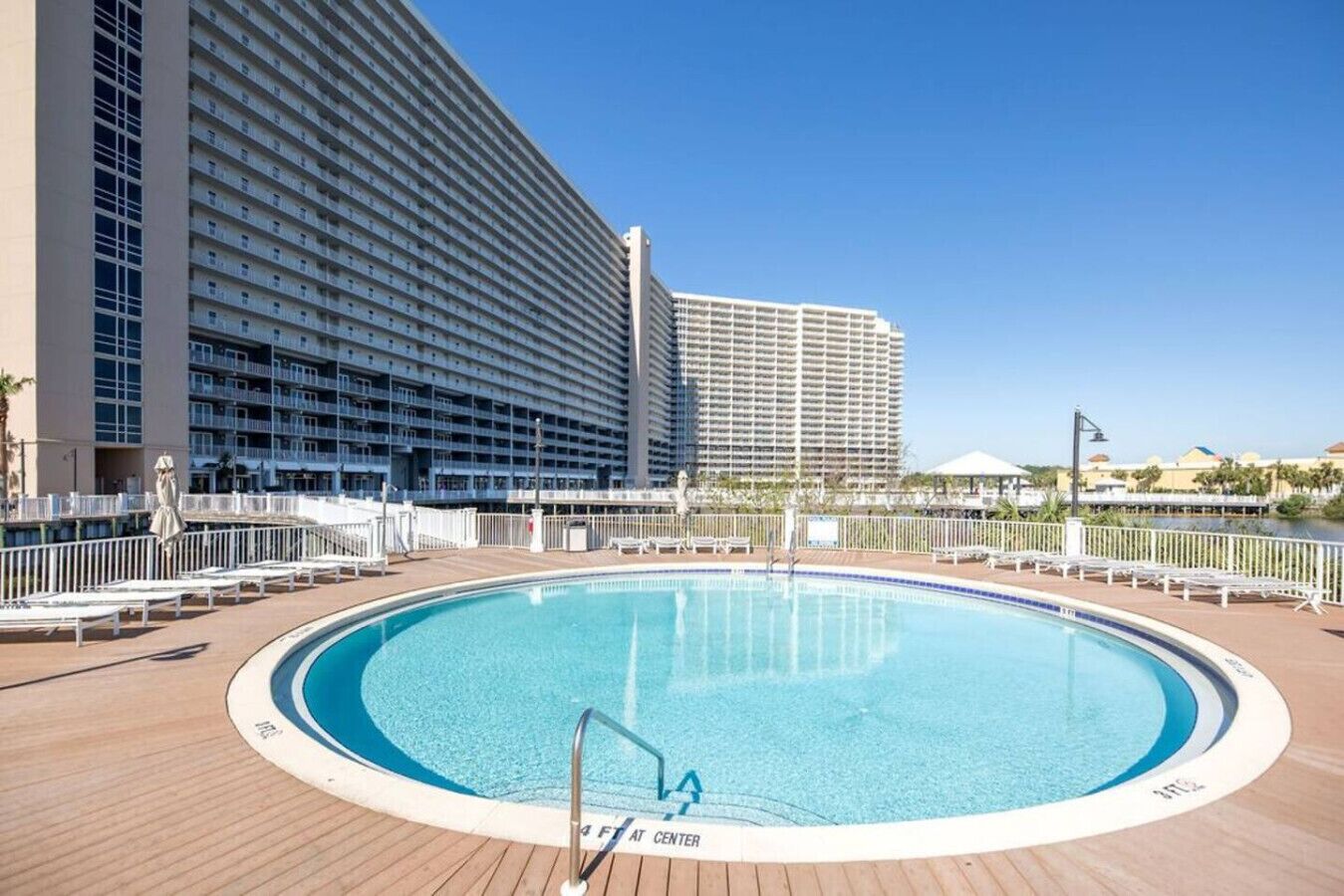 Et poolområde med en cirkulær pool, omgivet af liggestole og et hvidt hegn.