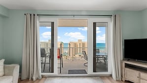 A balcony with a view of the ocean and buildings, a sofa, a TV, and a sliding door. - Living Right, Ocean View, 5 Pools, Beach Access at Laketown Wharf 1016 (Panama City Beach)