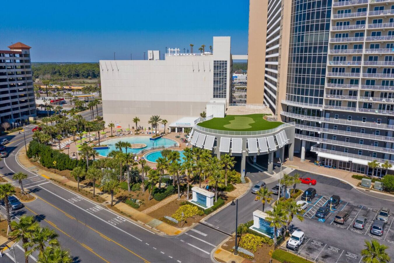 A hotel with a central courtyard featuring a swimming pool, surrounded by palm trees and a parking lot.