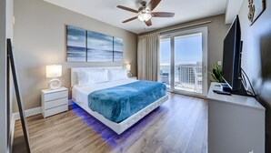 Une chambre moderne équipée d’un lit, de tables de chevet, d’un ventilateur de plafond, d’une télévision et d’un balcon avec vue.