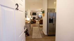A hallway leading to a kitchen with a refrigerator, a dining area with a table and chairs, and a living room with a sofa and a TV. - 3BR Fall Creek Condo Near Table Rock Lake + Branson Attractions | FC 39-2 (Branson)
