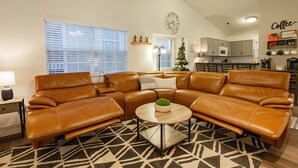 A living room with a brown leather sectional sofa, a round coffee table, and a patterned rug. There is a kitchen in the background with a clock and a 'Coffee' sign on the wall. - 3BR Fall Creek Condo Near Table Rock Lake + Branson Attractions | FC 39-2 (Branson)