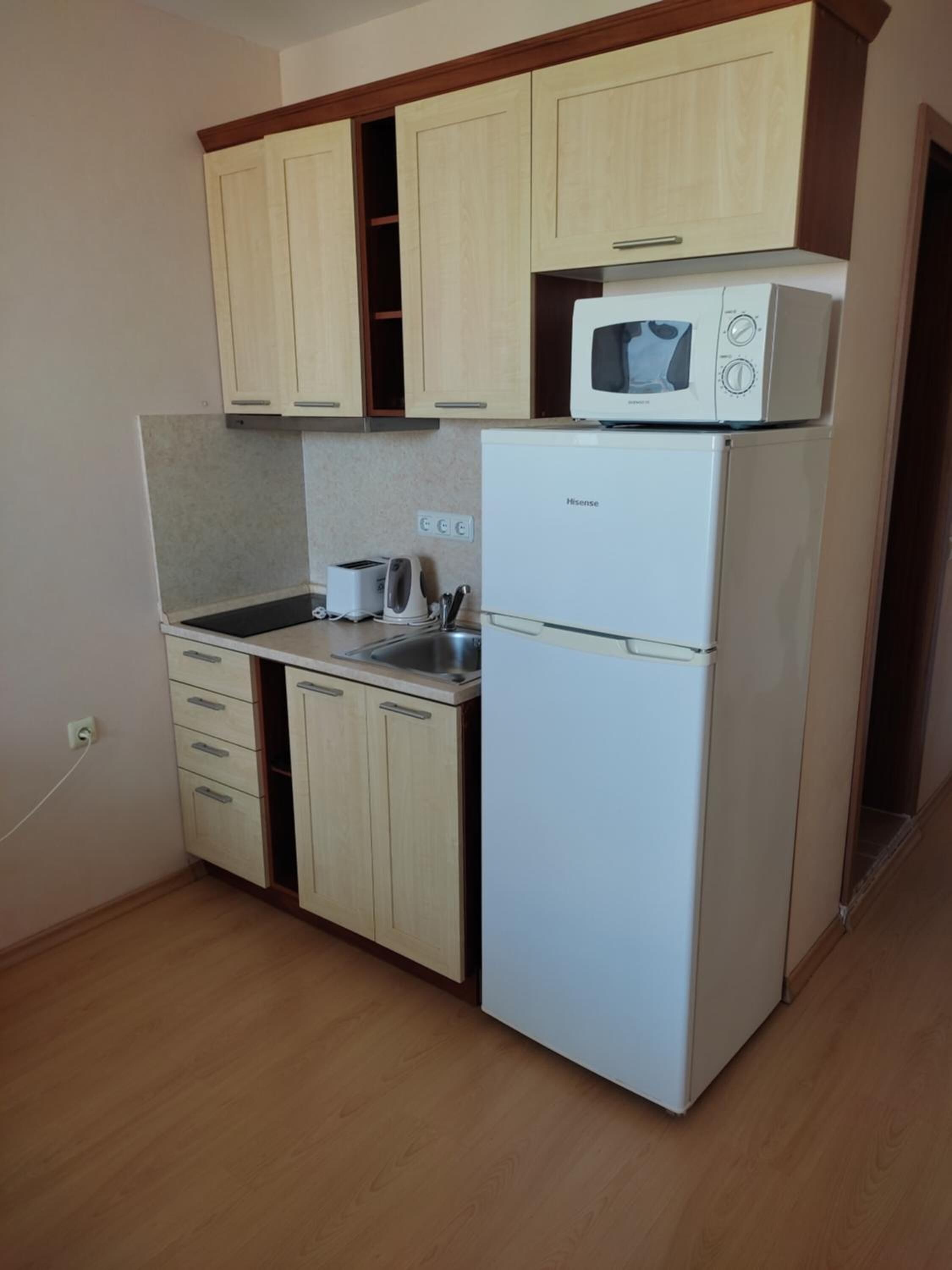 A compact kitchen with wooden cabinets, a white refrigerator, a microwave, a toaster, and a sink.