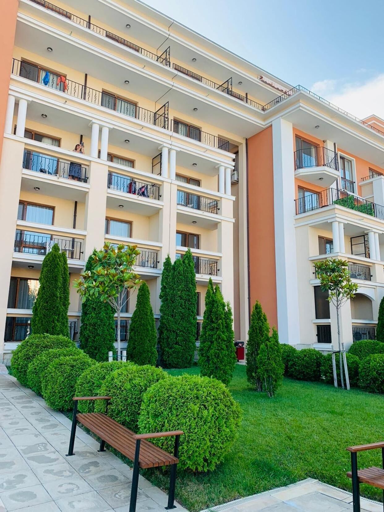 A multi-story hotel with balconies, a well-maintained lawn, and benches.