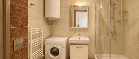 Un baño moderno con inodoro, lavadora, lavabo y ducha con mampara de vidrio.