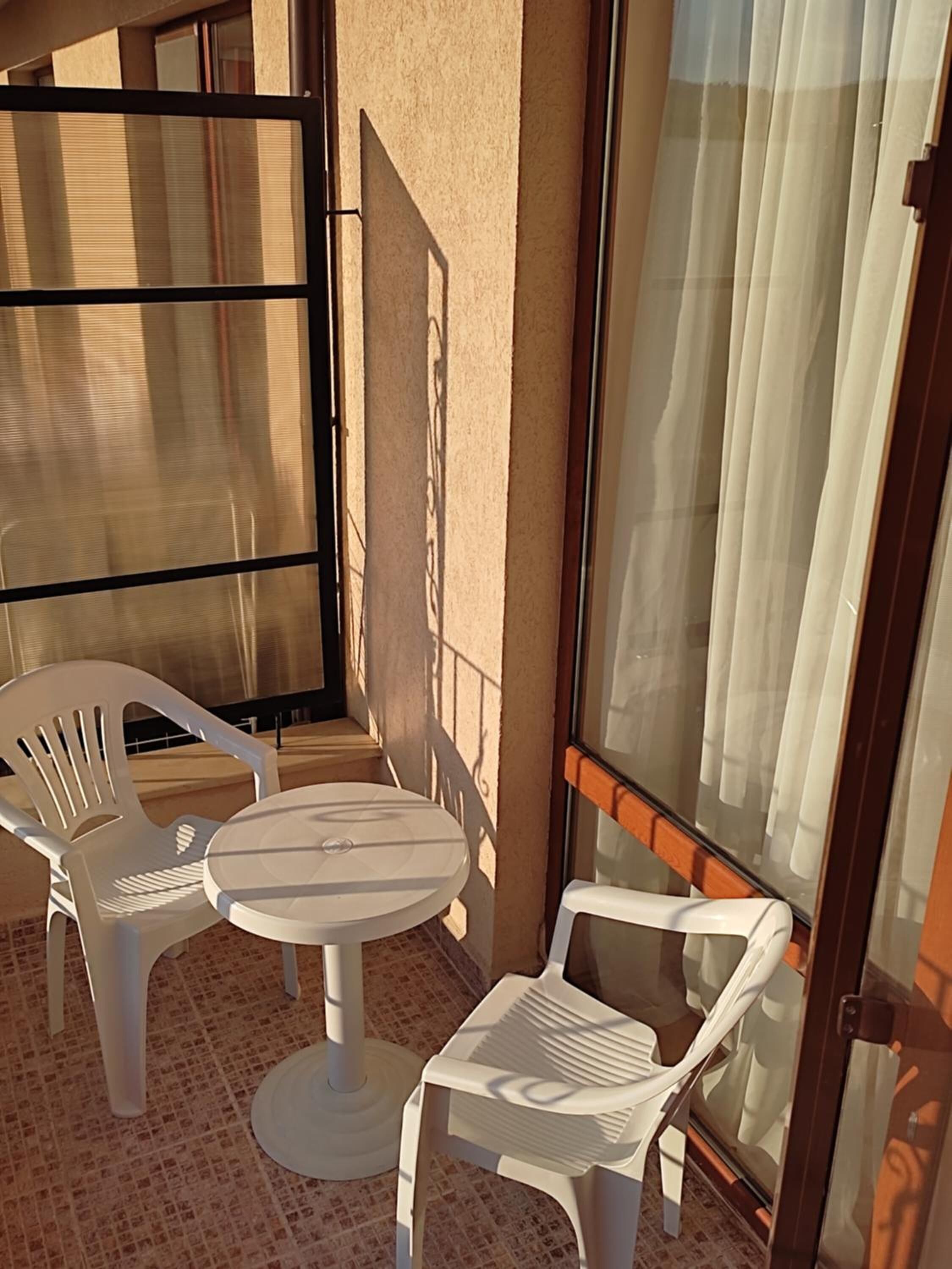 A small outdoor seating area with a round table and two chairs, a glass door, and a view of the outside.