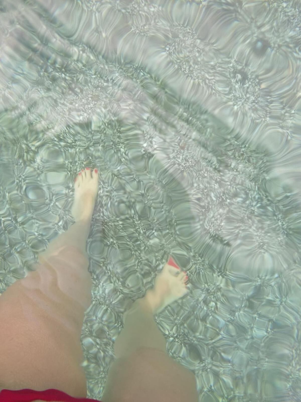 A person's legs in a bathtub with clear water.