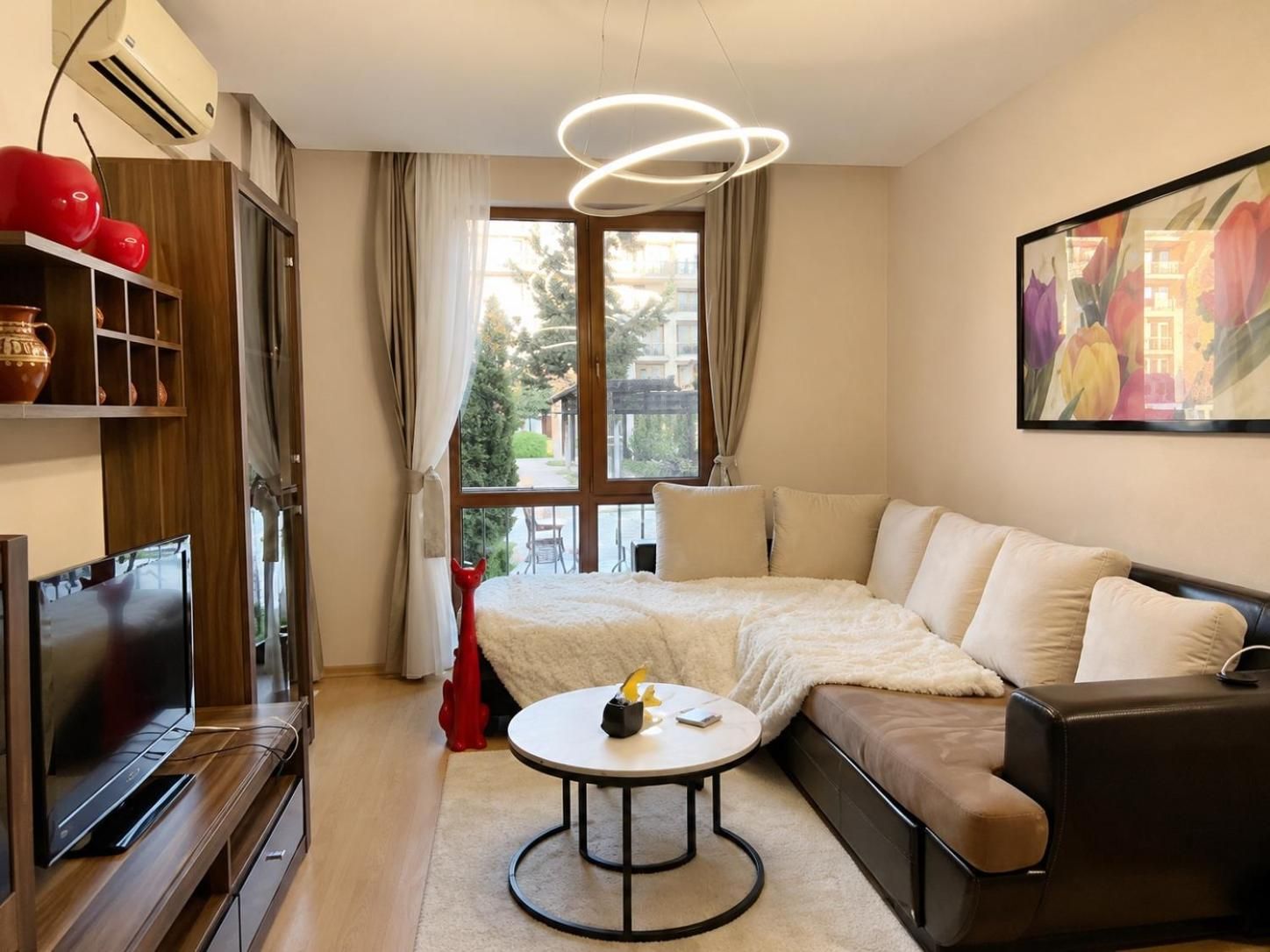 A modern living room with a sofa, a coffee table, a television, and a large window with curtains.