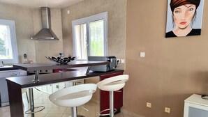 Una cocina moderna con una isla central, dos taburetes blancos de bar, una campana extractora de acero inoxidable y un cuadro en la pared.