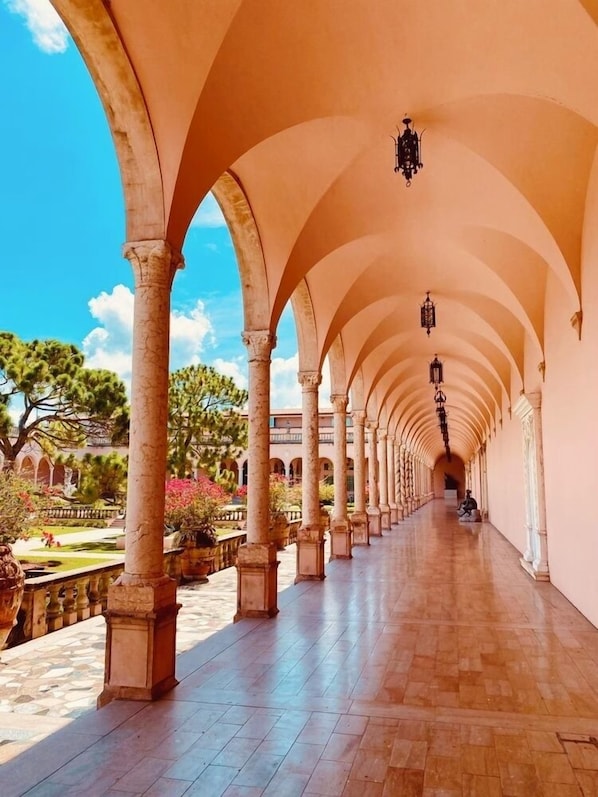 A long corridor with arches, potted plants, and a clear sky.