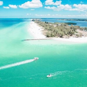 An aerial view of a coastal area with clear turquoise waters, a sandy beach, and a small island with vegetation. - Heated Pool~Massive Spanish Home~Water Views~Sunset Deck~Grill~WIFI~Near Beaches (Bradenton)