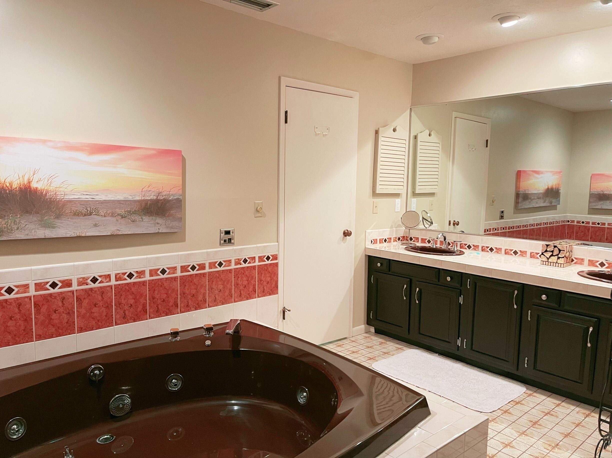 Un baño con una bañera grande, un lavamanos y un espejo. Hay azulejos decorativos en la pared y un cuadro sobre la bañera.