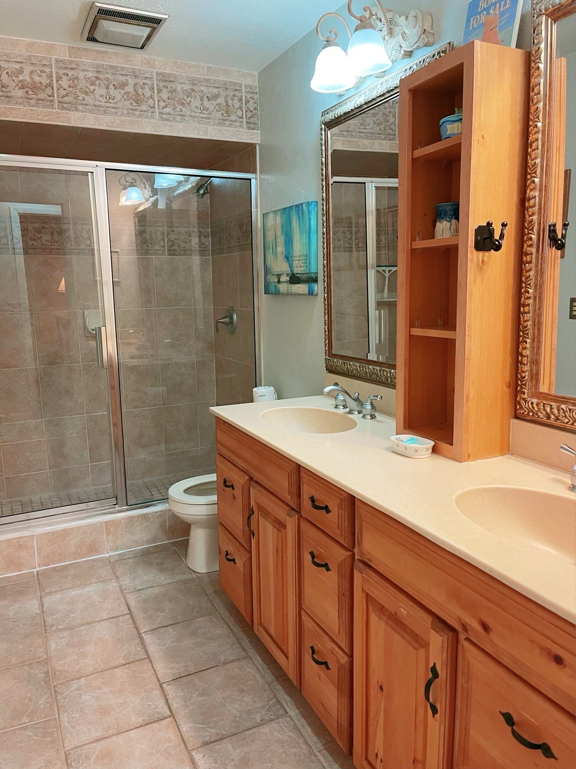 A bathroom with a glass shower enclosure, a sink with a mirror, wooden cabinets, and a toilet.