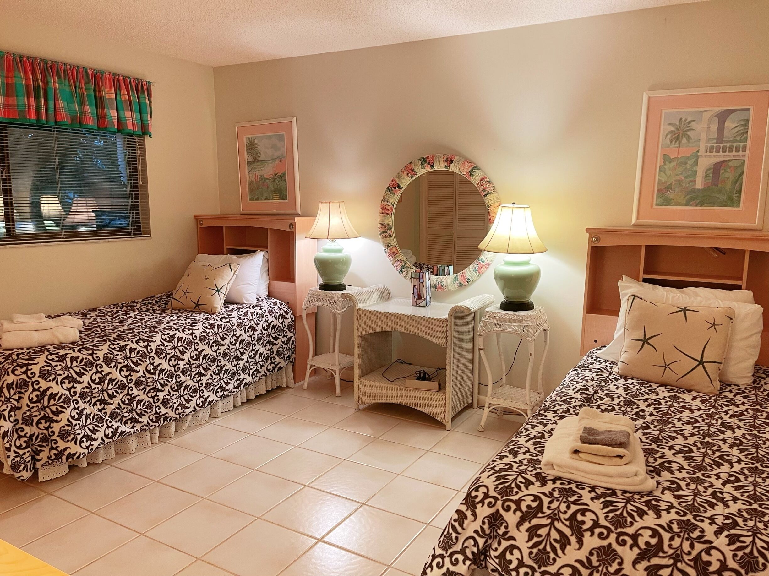 A hotel room with two beds, a vanity with a mirror, and a small table with a lamp.