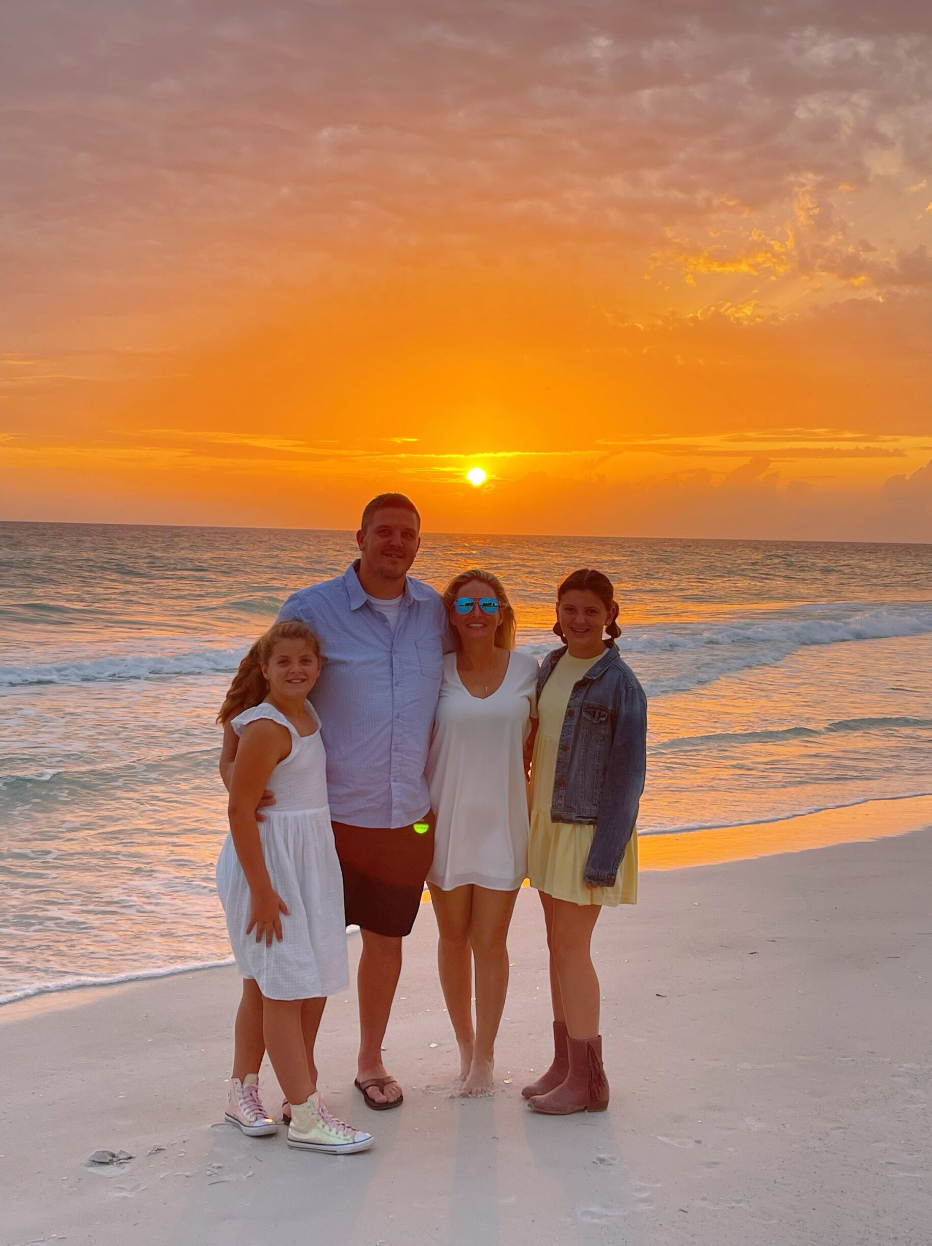 Une famille de quatre personnes se tient sur une plage, avec un coucher de soleil en arrière-plan.