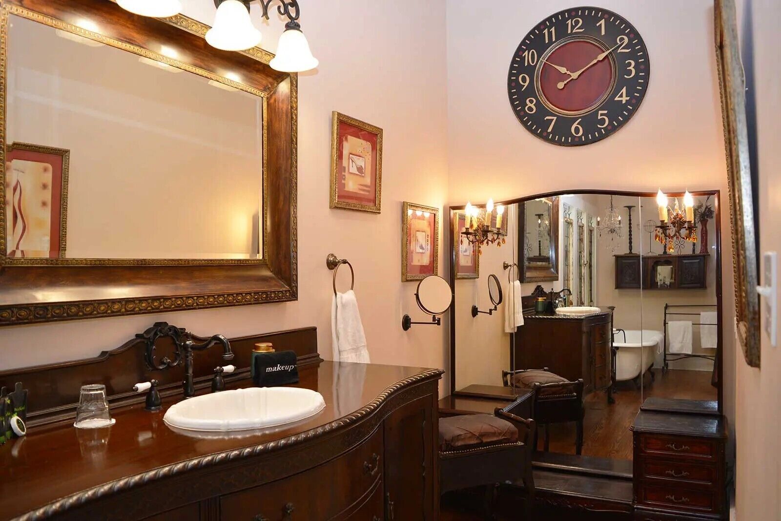 A classic bathroom with a large mirror, a round wall clock, and a vanity with a sink and towel rack.