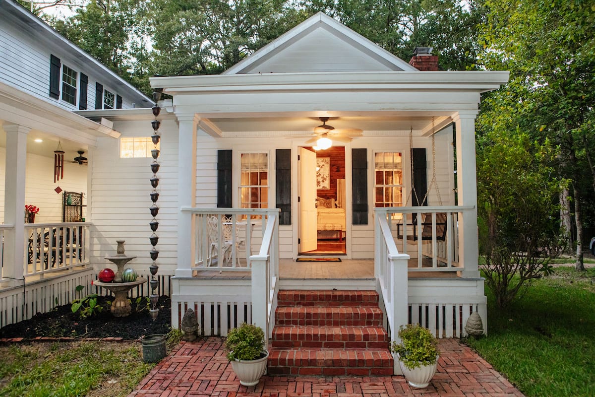 A white house with a porch, steps, and a door leading to an interior.