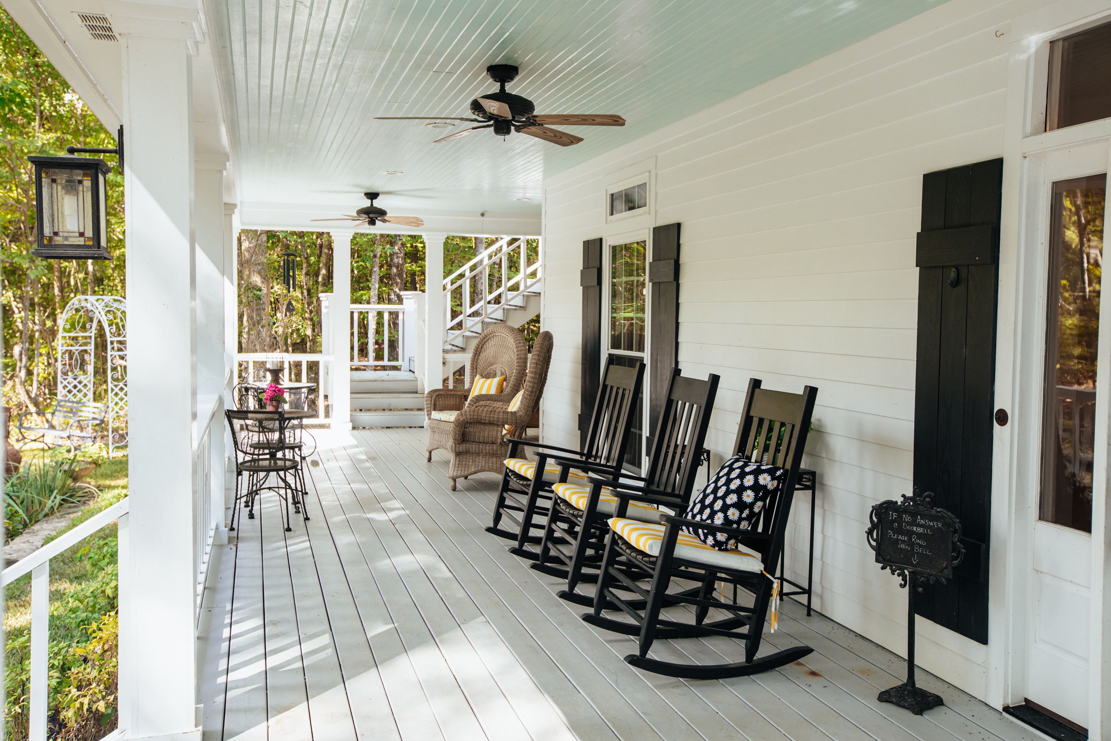 A white porch with rocking chairs, a table, and a sign.