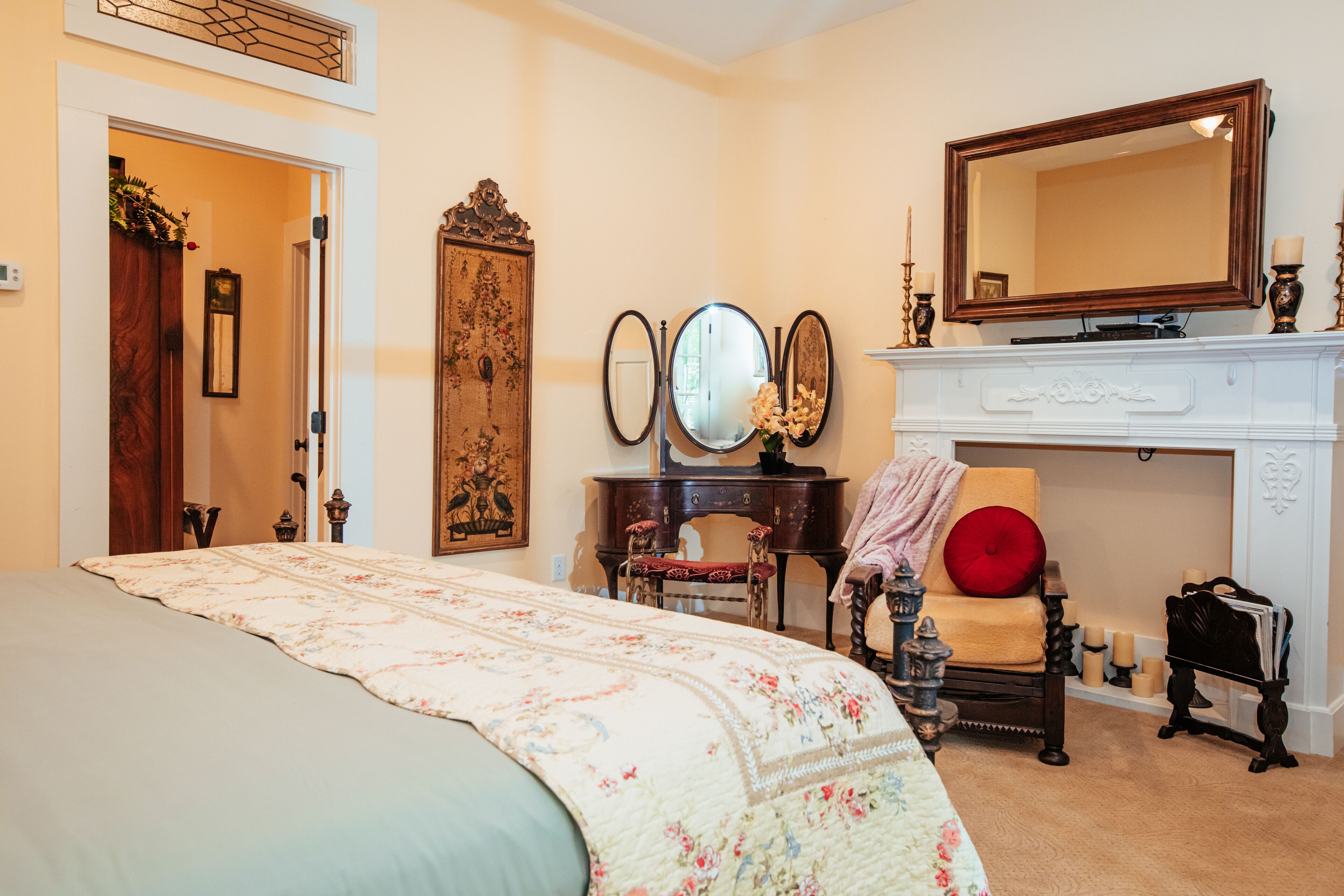 Un dormitorio con cama, cómoda, espejo, silla y chimenea.