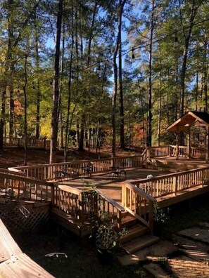A wooden deck with a gazebo, surrounded by tall trees.