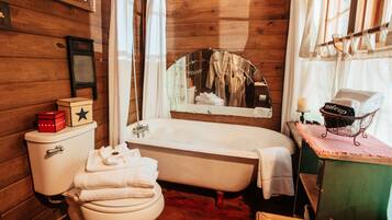 A wooden cabin bathroom with a bathtub, toilet, and a mirror with a towel hanging on it.