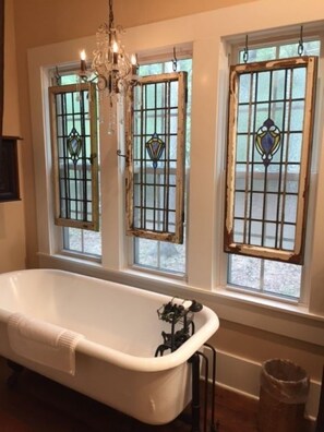 A bathroom with a white bathtub, a chandelier, and three windows with stained glass.