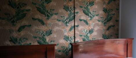 A hotel room with two wooden beds, a large window, and a wall with a tropical leaf pattern.