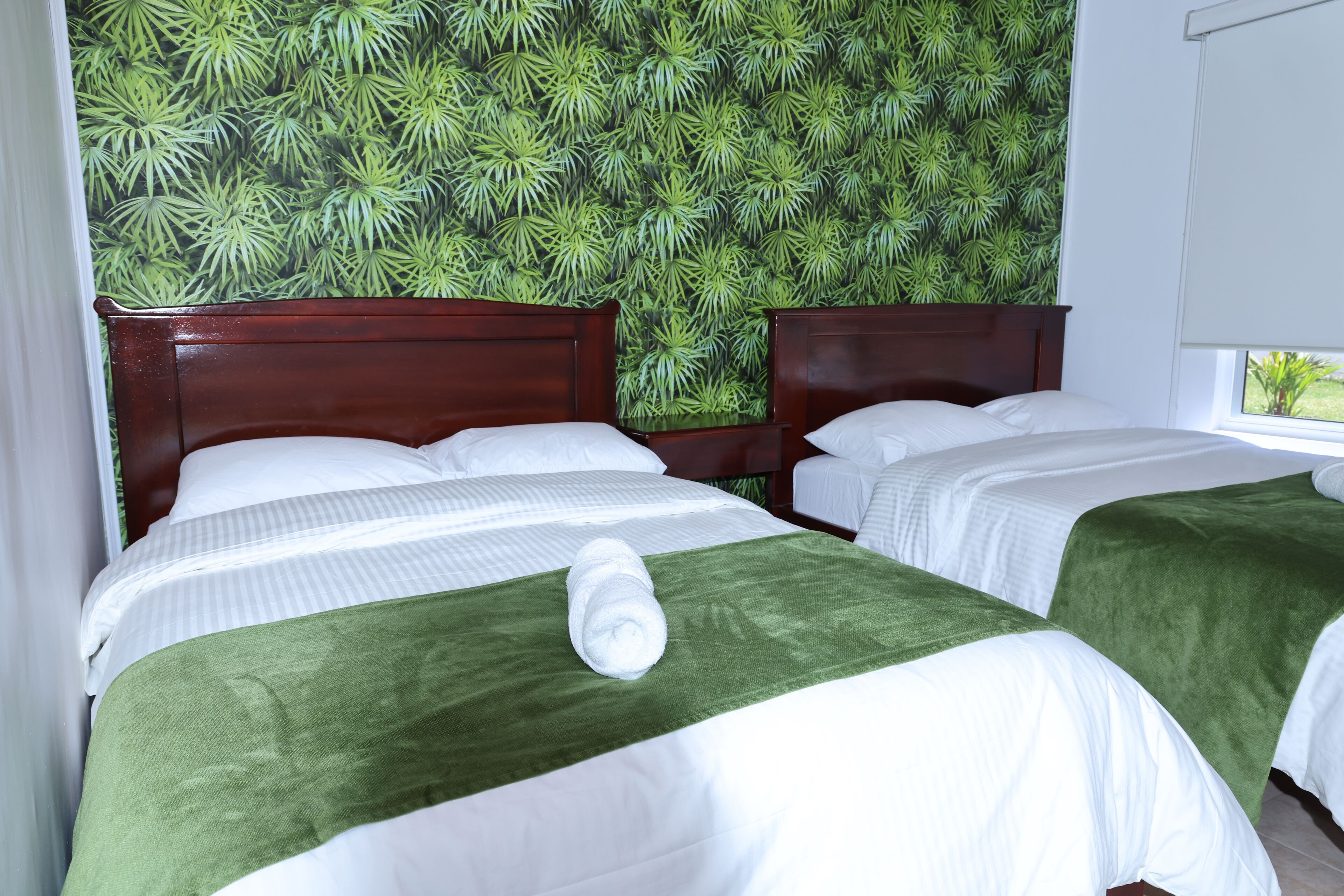 Habitación de hotel con dos camas, cada una con cubrecama verde y ropa de cama blanca.