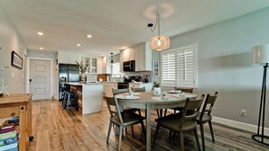 A modern kitchen with white cabinets, a stainless steel refrigerator, and a dining area with a wooden table and chairs.