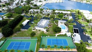 An aerial view of a residential area with two tennis courts, a swimming pool, and a large building with a flat roof. - Tranquil West Bay Point and Moorings Community (Holmes Beach)