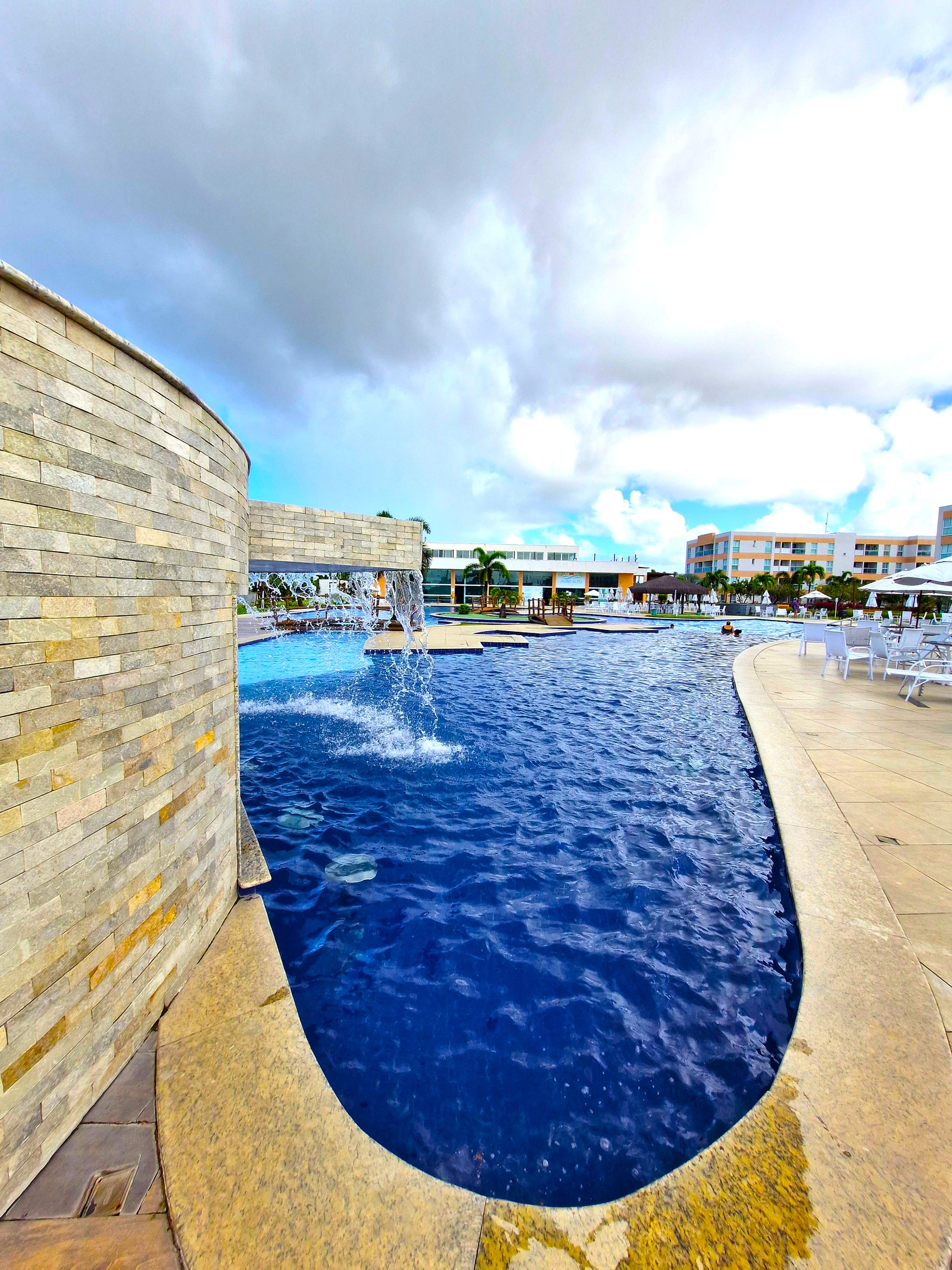 A swimming pool with a curved edge, surrounded by a stone wall and a tiled deck.