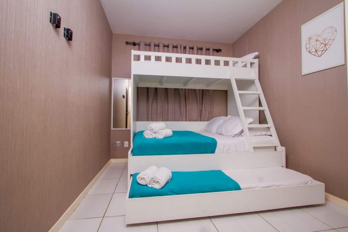 Une chambre avec un lit superposé, une échelle, deux lits et une lampe fixée au mur.