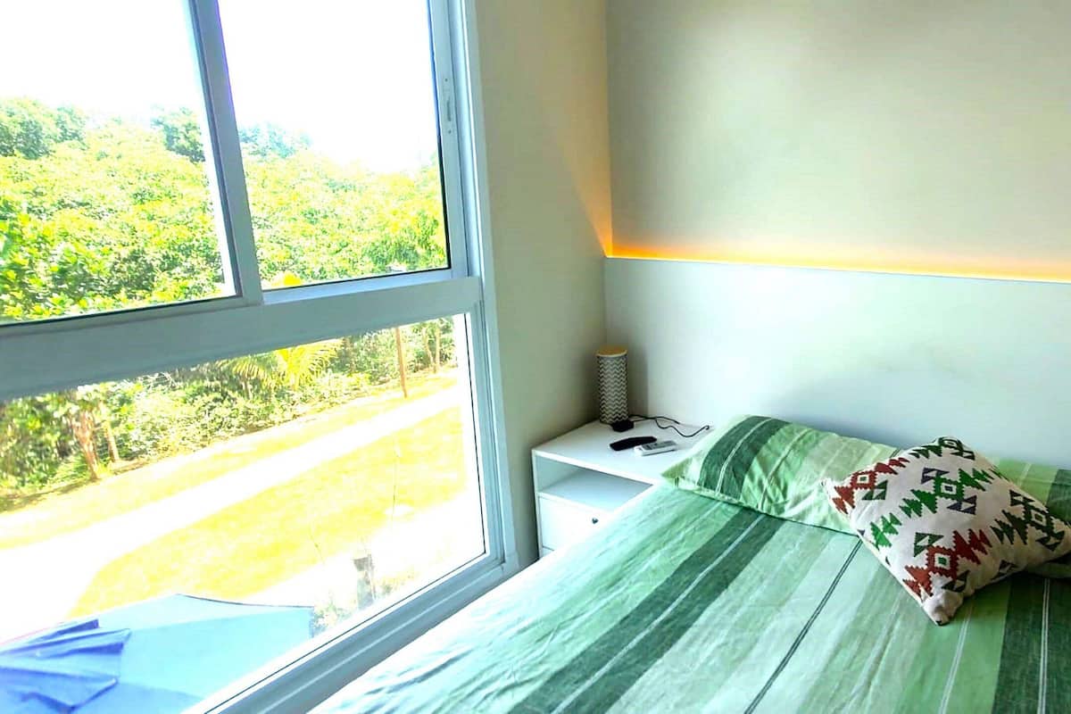 Une chambre avec un lit, une table de chevet, une lampe et une fenêtre donnant sur un paysage verdoyant.