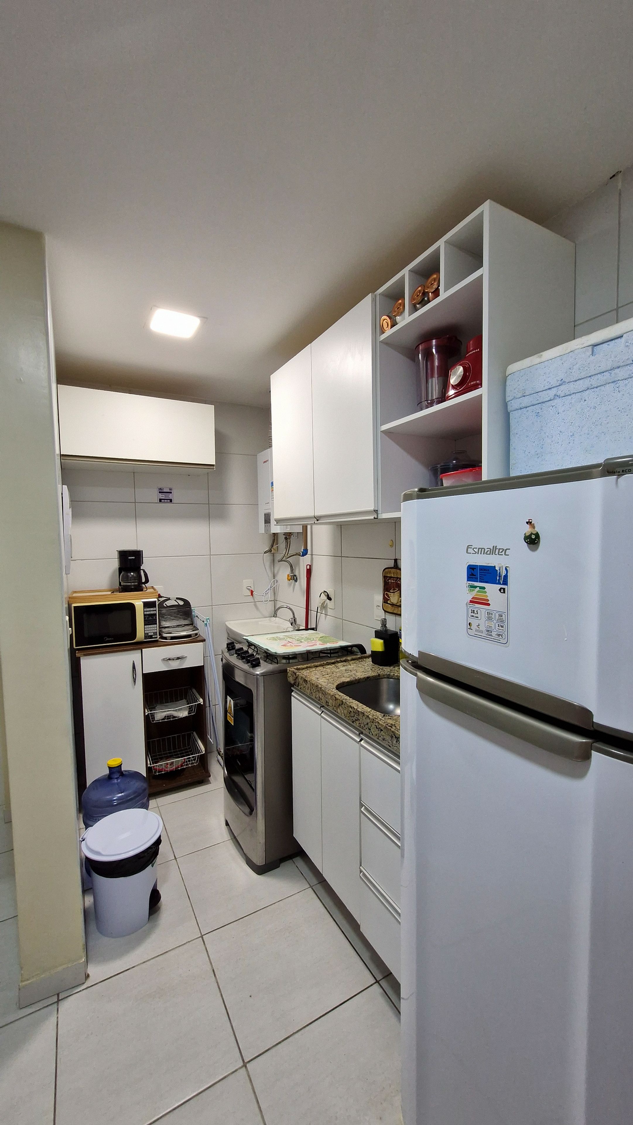 Een kleine keuken met witte kasten, een ingebouwde magnetron, een gasfornuis en een koelkast.