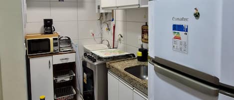 Una cocina compacta con alacenas blancas, microondas integrado, estufa a gas y refrigerador.