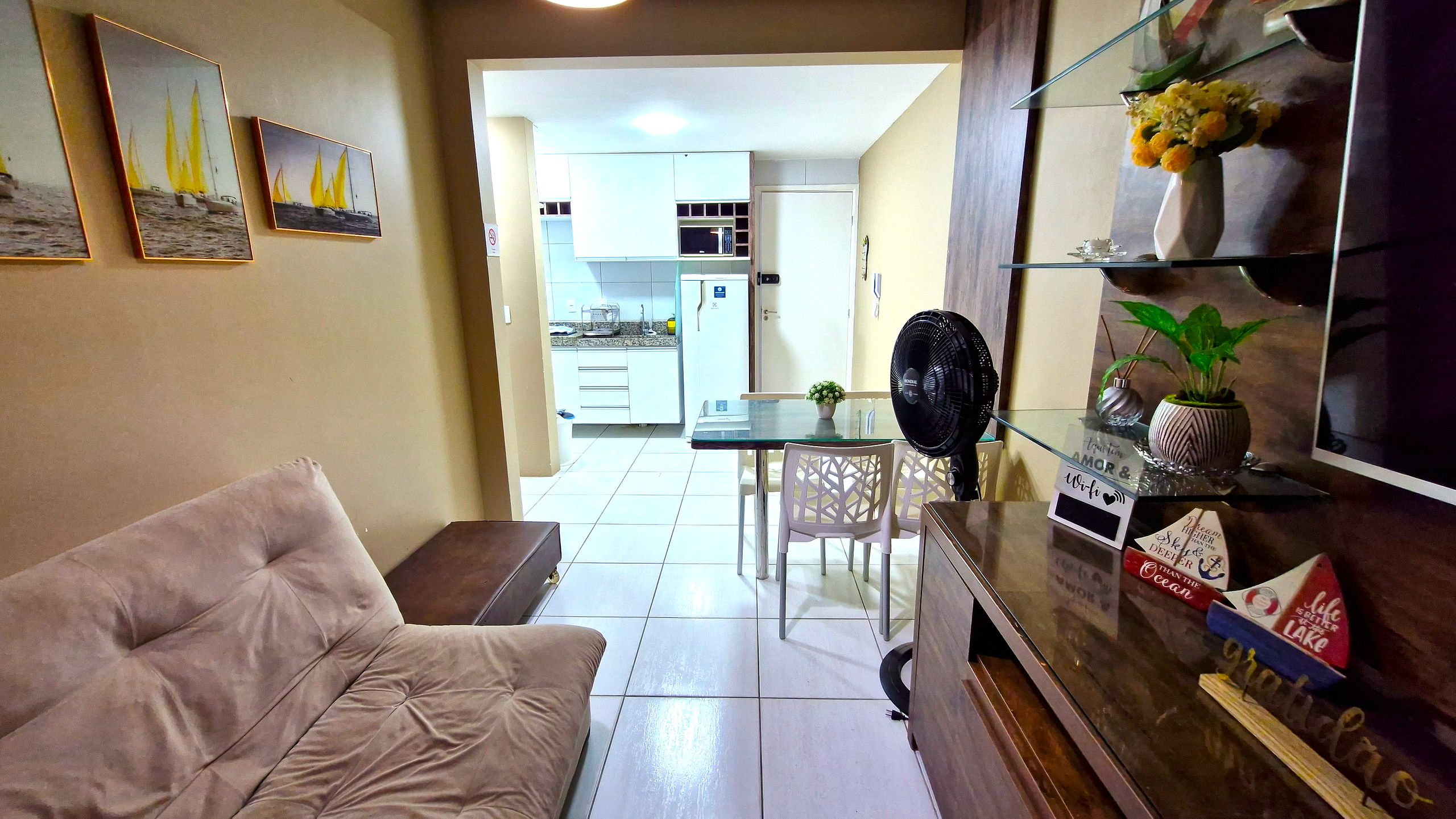 A living room with a sofa, a dining table with chairs, a kitchen in the background, and a TV on a stand.