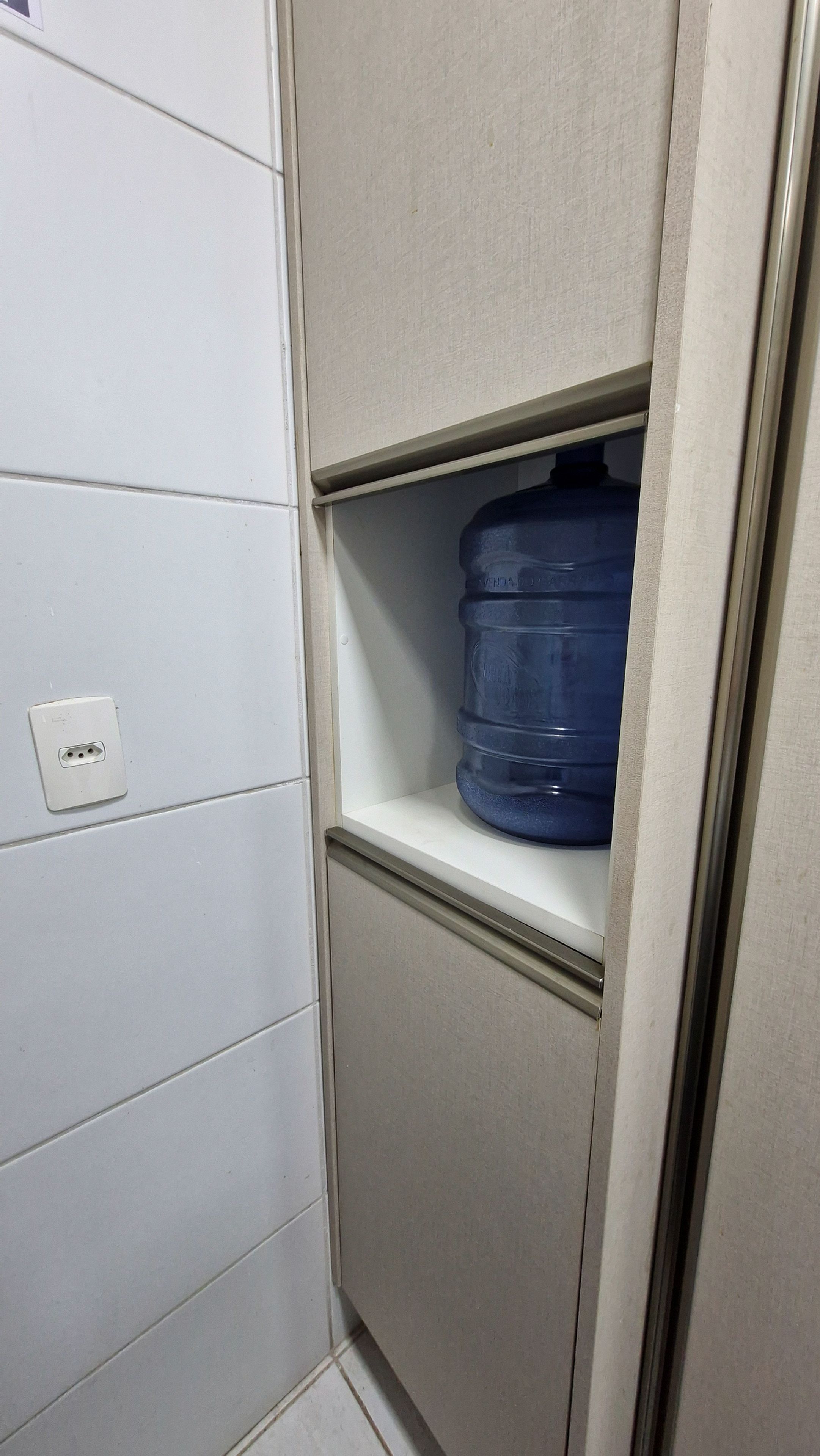 Un baño con pared de azulejos blancos, repisa blanca y un recipiente azul para agua.