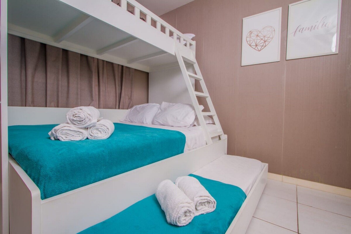 Une chambre avec un lit superposé, une échelle, deux serviettes enroulées et deux tableaux encadrés accrochés au mur.