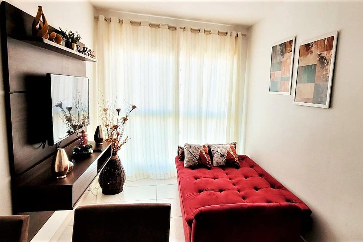 Un salon avec un canapé rouge, un téléviseur, une table basse et une fenêtre avec des rideaux.