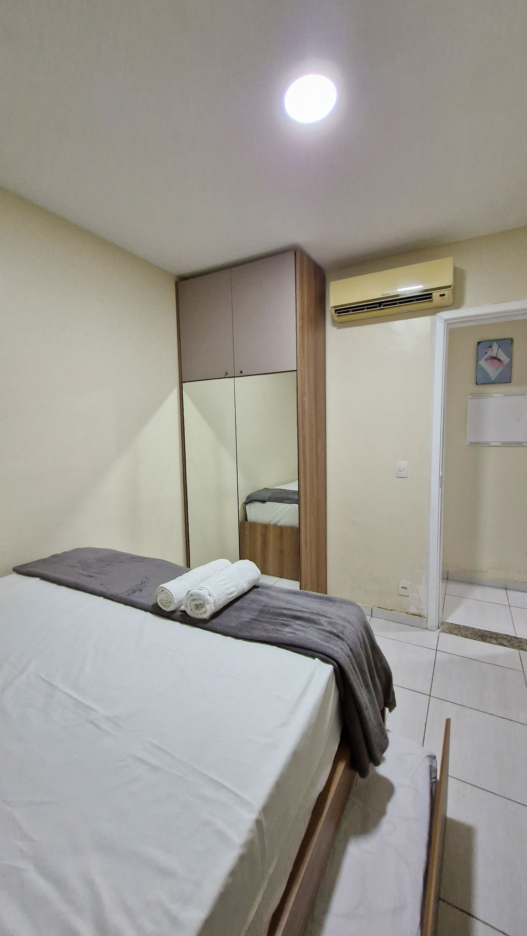 A bedroom with a bed, a wardrobe, an air conditioning unit, and a door.