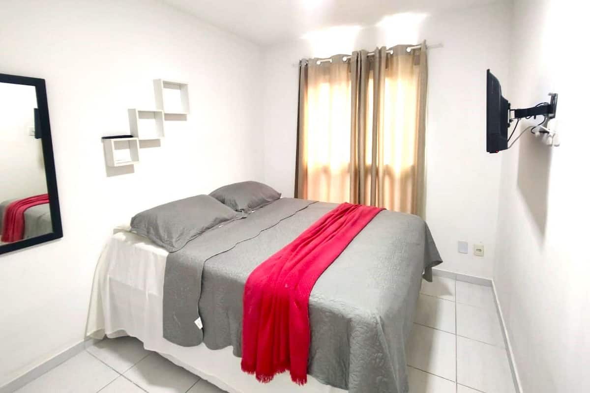 Une chambre à coucher avec un lit, un miroir, une télévision et une fenêtre avec des rideaux.