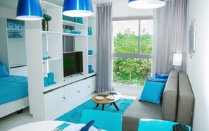 Un salon avec un téléviseur, des meubles bleus, une fenêtre donnant sur un beau paysage et un canapé.