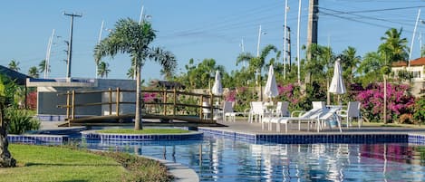A swimming pool with lounge chairs and umbrellas, surrounded by palm trees and a tiled deck.