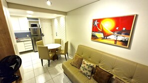 Un salon avec un canapé, une table à manger avec des chaises, un coin cuisine avec un réfrigérateur et un tableau accroché au mur.
